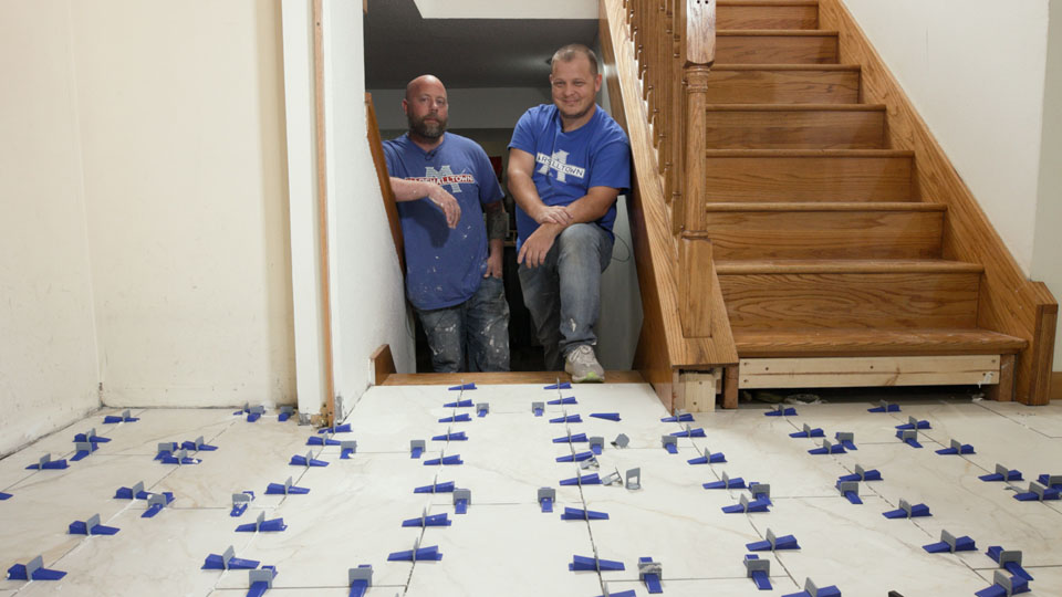 two guys smiling in front of their tiled entryway after installing a leveling system